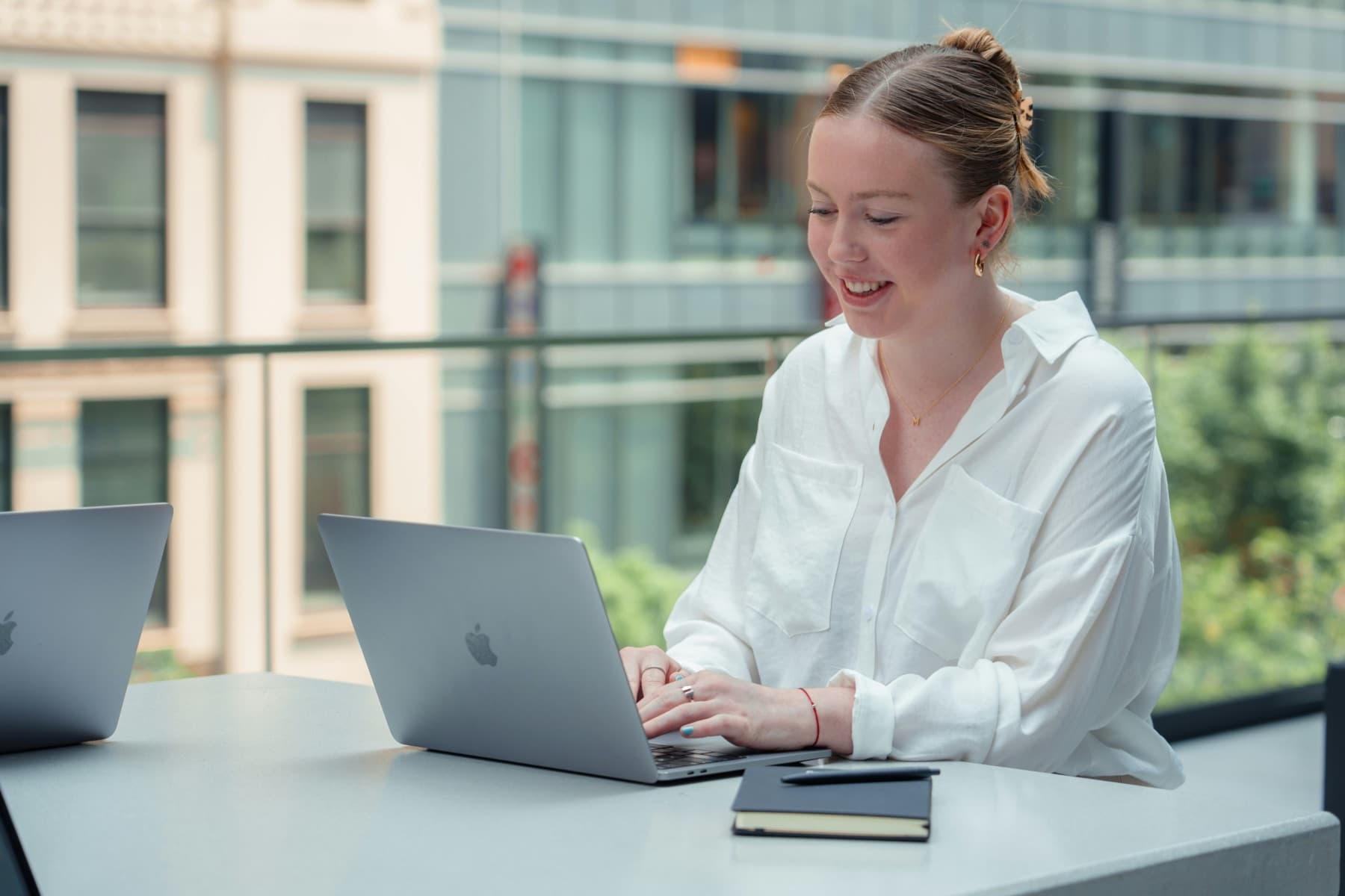 A person smiling at a laptop on a sunny office terrace